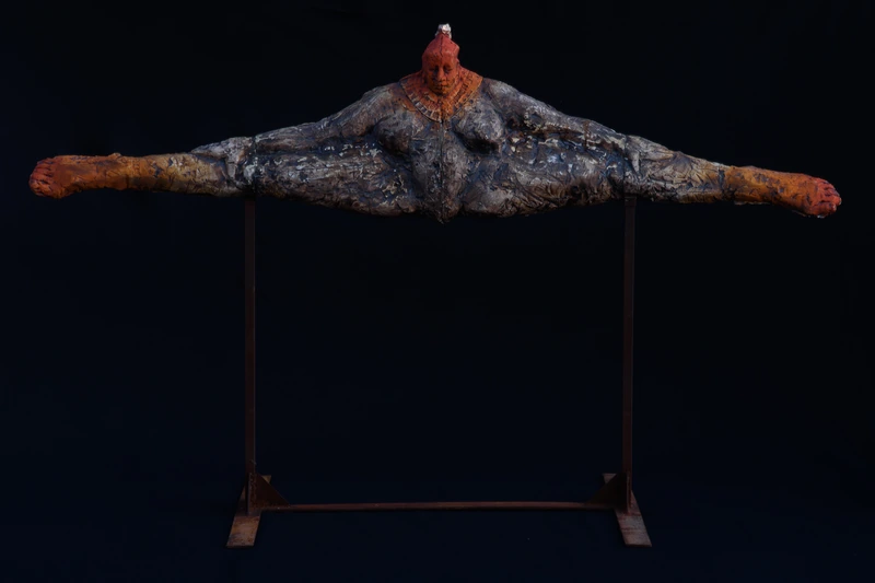 黒い背景に、左右へ大きく広がる彫刻作品。表面の凹凸と褐色・灰色の質感。